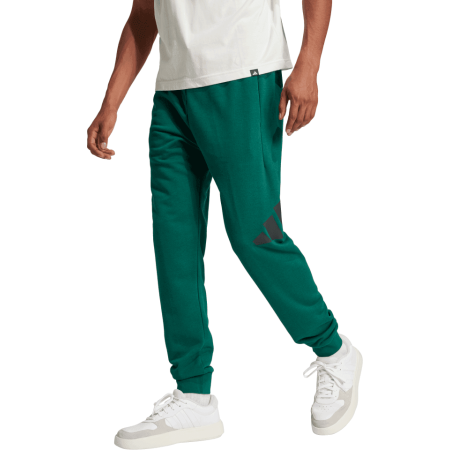 Adidas žalios vyriškos treninginės kelnės JE8971 su baltu logotipu ir siaurėjančiu siluetu.